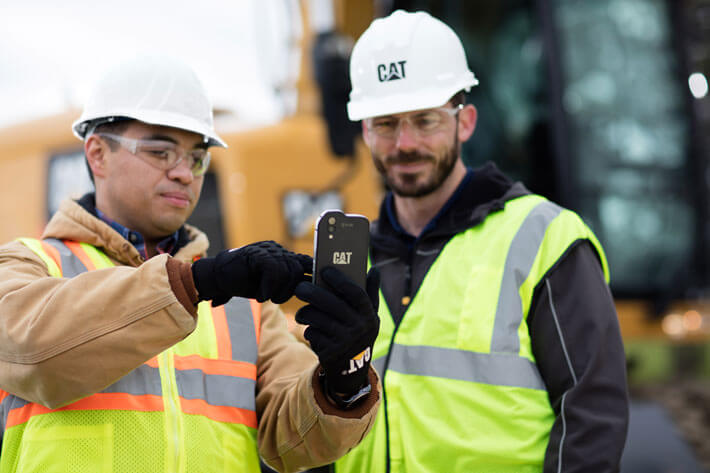 two men in ppe on jobsite looking at smart phone